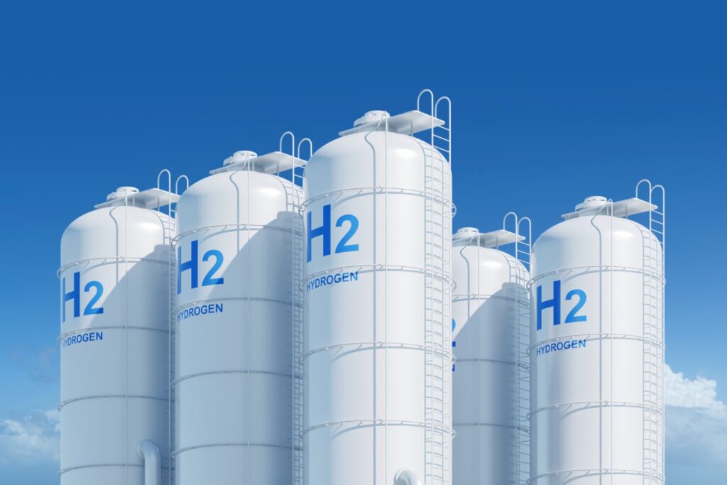 White vertical hydrogen storage tanks marked H2 against a blue sky