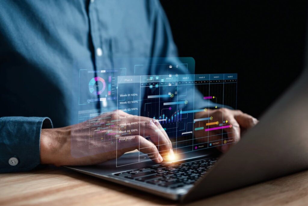 Hands typing on a laptop, with a project schedule shown as a holographic Gantt chart